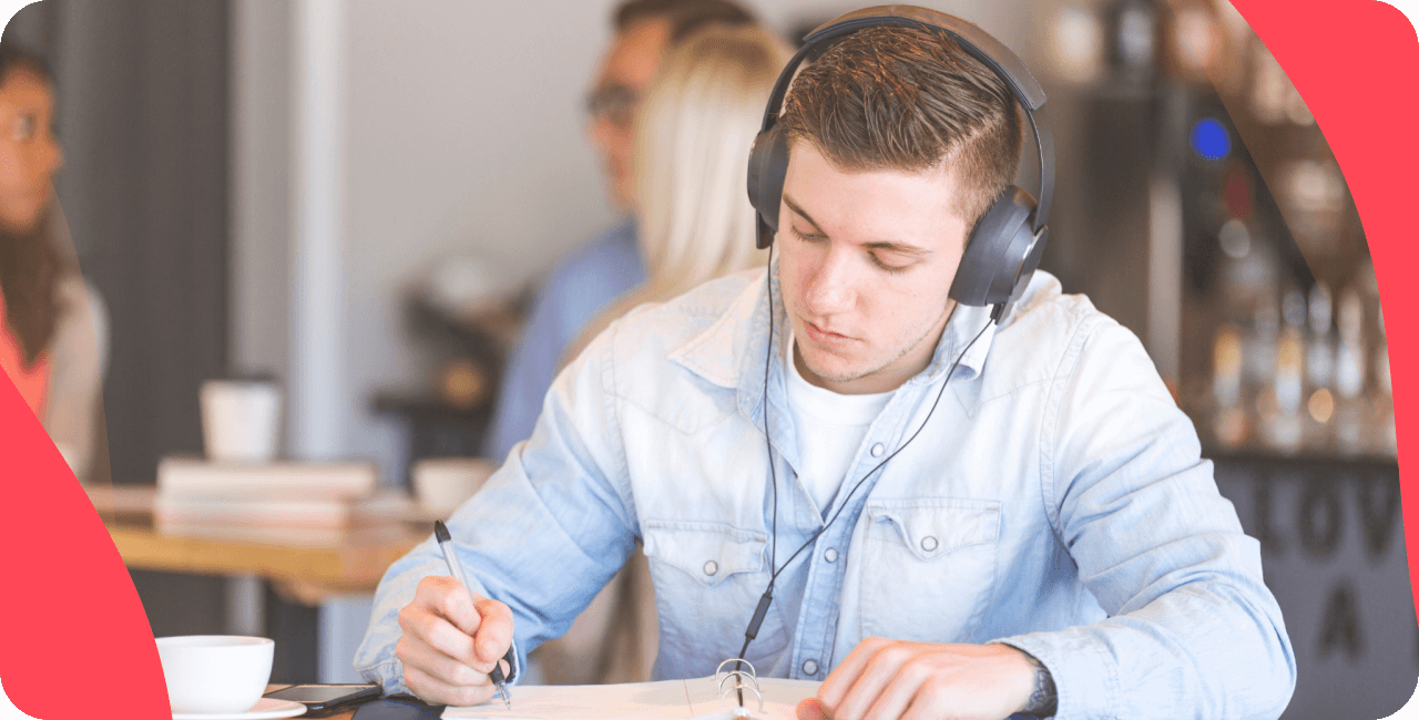 Man with headphones, listening to music and writing in a notepad.